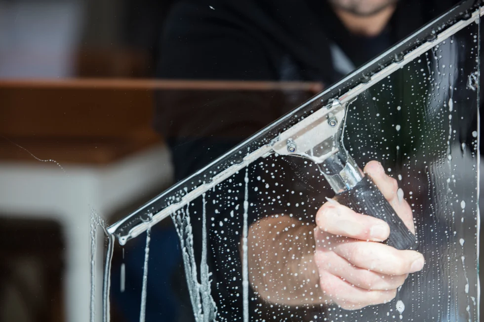Fönsterputs med fönsterskrapa på vått glas